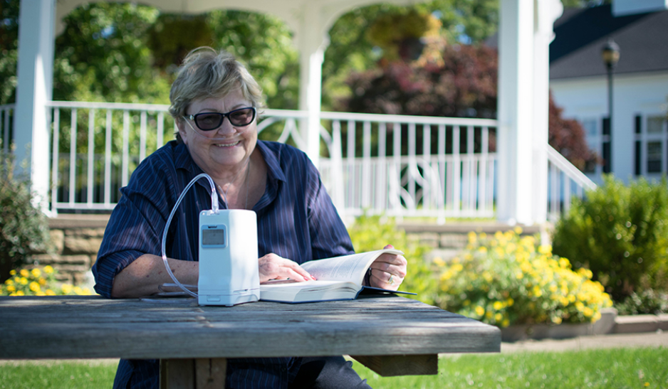 Happy and healthy elderly woman at the park reading a book with her OxyGo portable oxygen concentrator.