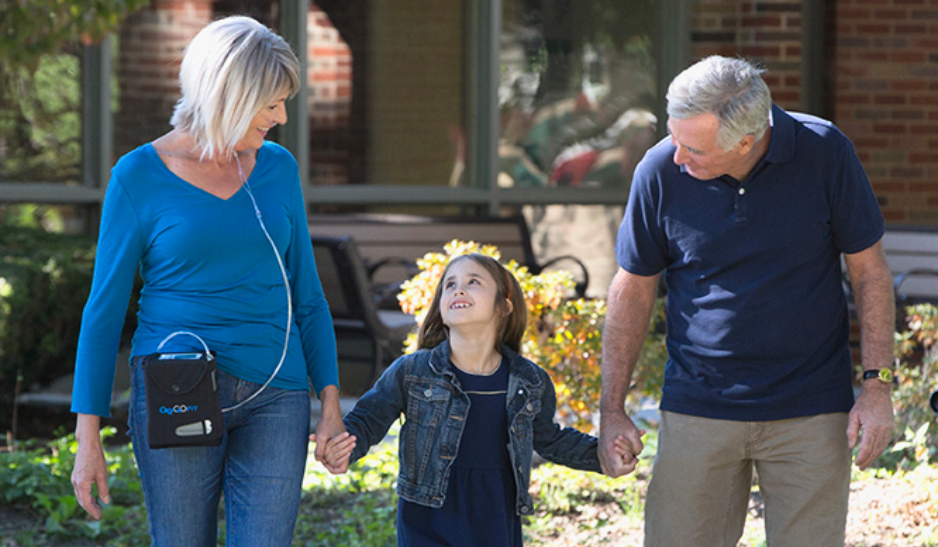 A Grandpa and Grandma who is on oxygen, walking and holding hands with their young Granddaughter